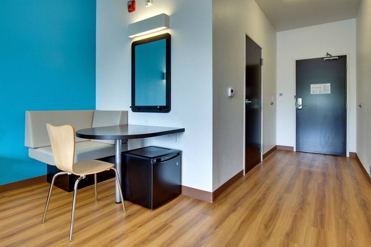 Una habitación de hotel moderna con una mesa redonda, una silla, un mueble negro pequeño y un espejo en la pared.