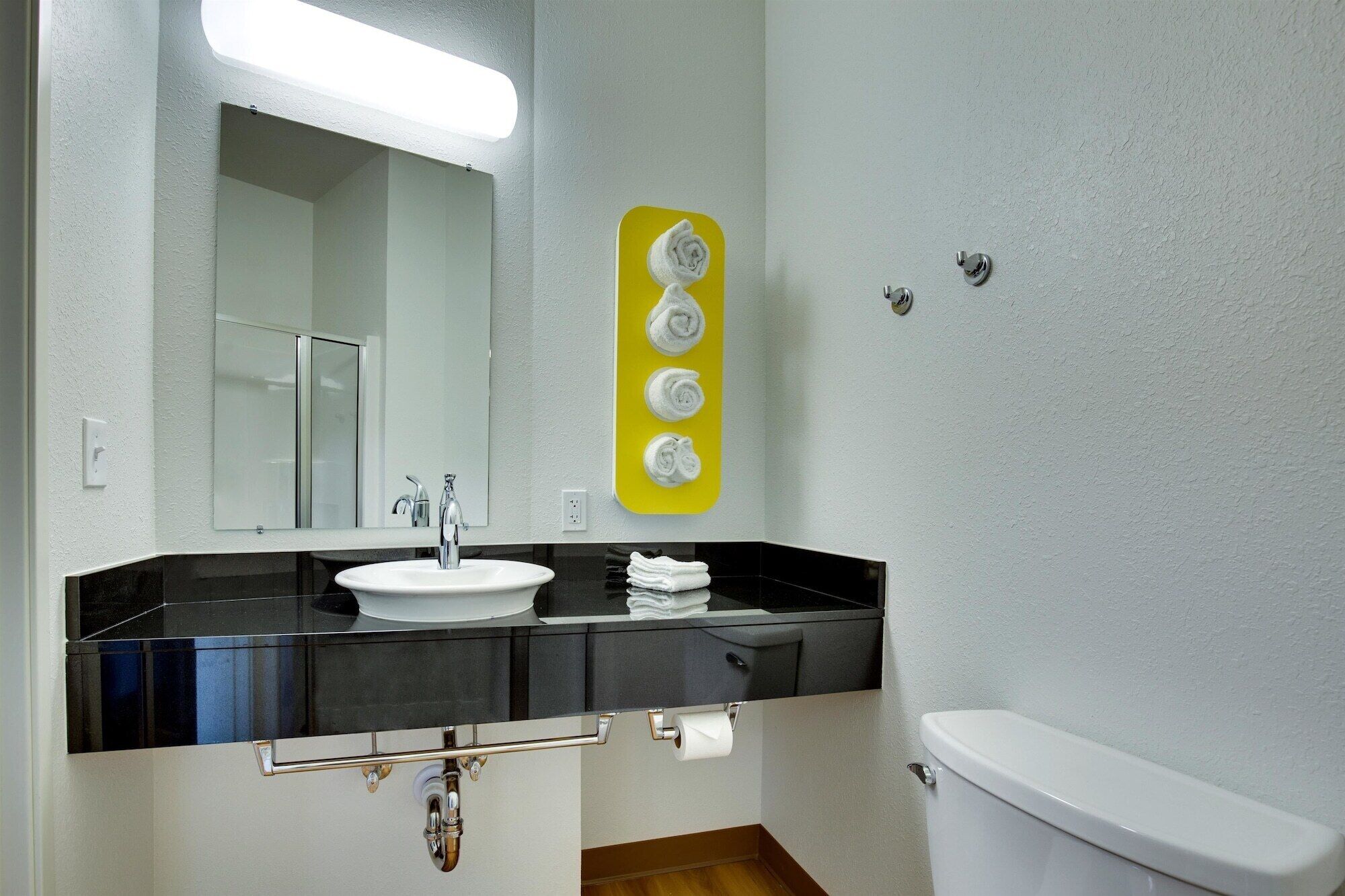 A bathroom with a white sink, black countertop, and a yellow towel rack.