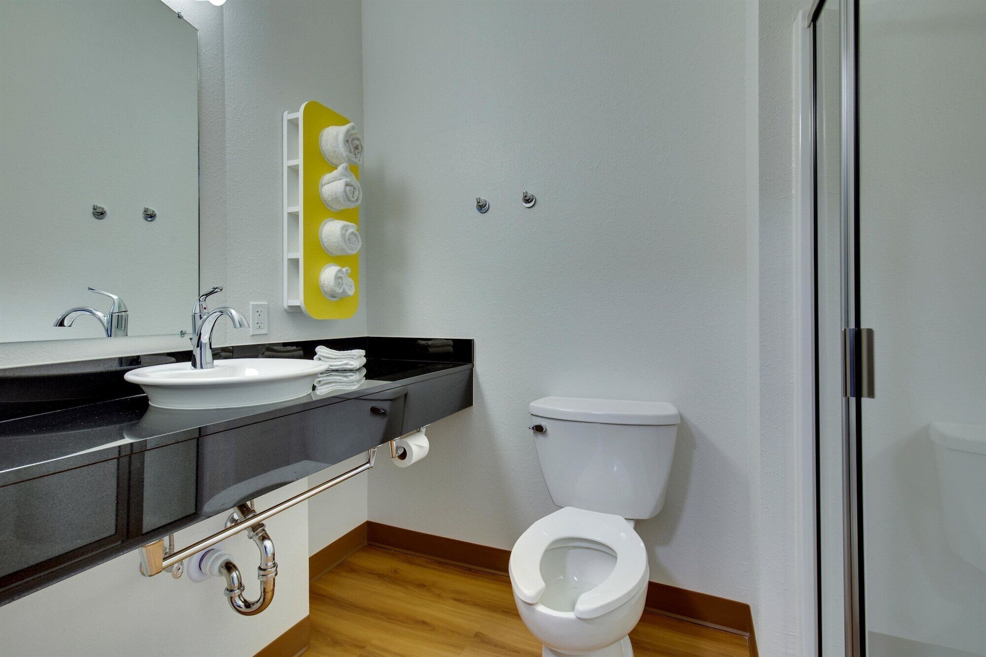 Een moderne badkamer met een wit wastafelmeubel, een spiegel, een toilet en een gele handdoekhouder.