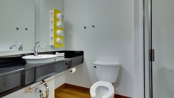 Een moderne badkamer met een wit wastafelmeubel, een spiegel, een toilet en een gele handdoekhouder.