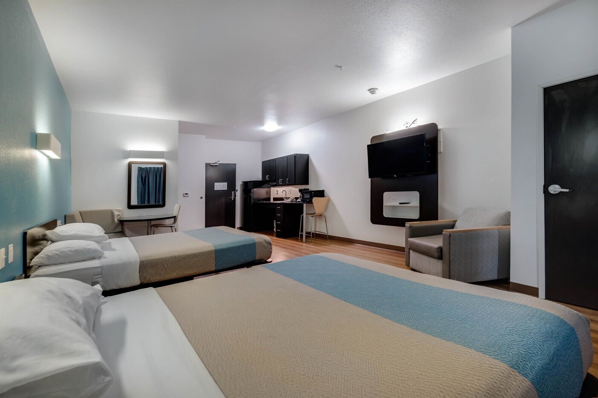 A hotel room with two beds, a kitchenette, a TV, and a seating area.