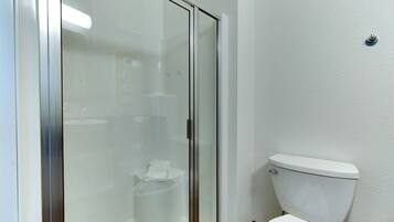 A bathroom with a glass shower enclosure, a toilet, and a white wall.