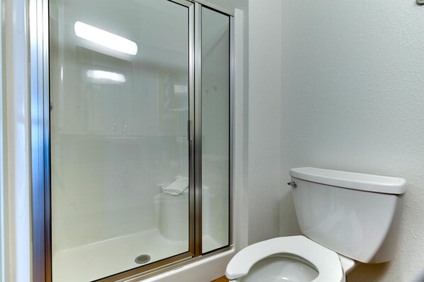 Un baño con ducha envuelta en vidrio, un inodoro blanco y un lavabo blanco.