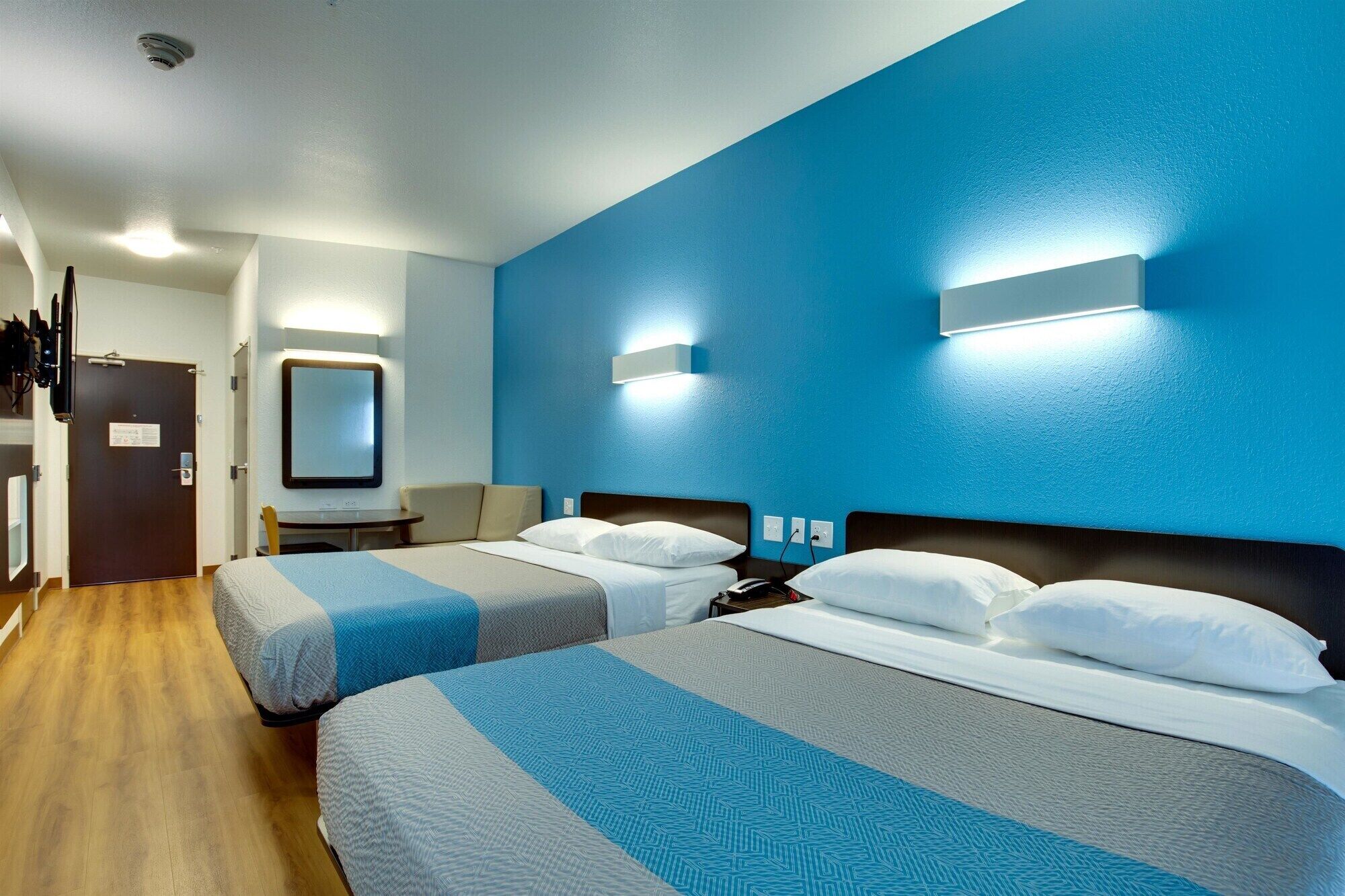 A hotel room with two beds, a desk, a chair, and a TV.