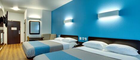 A hotel room with two beds, a desk, a chair, and a TV.