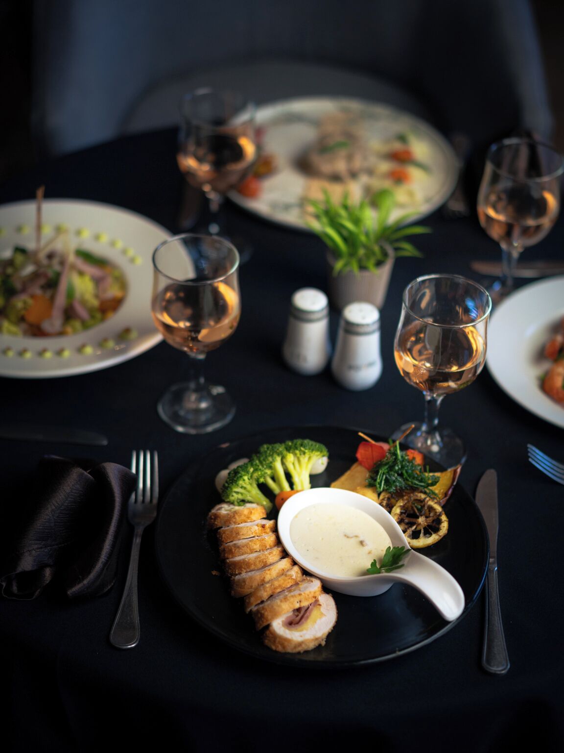 Une table à manger dressée avec des assiettes remplies de nourriture, des verres de vin et des couverts.