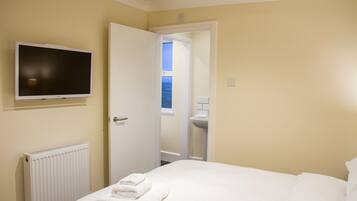 A hotel room with a bed, a TV mounted on the wall, a radiator, and a bathroom visible through an open door.