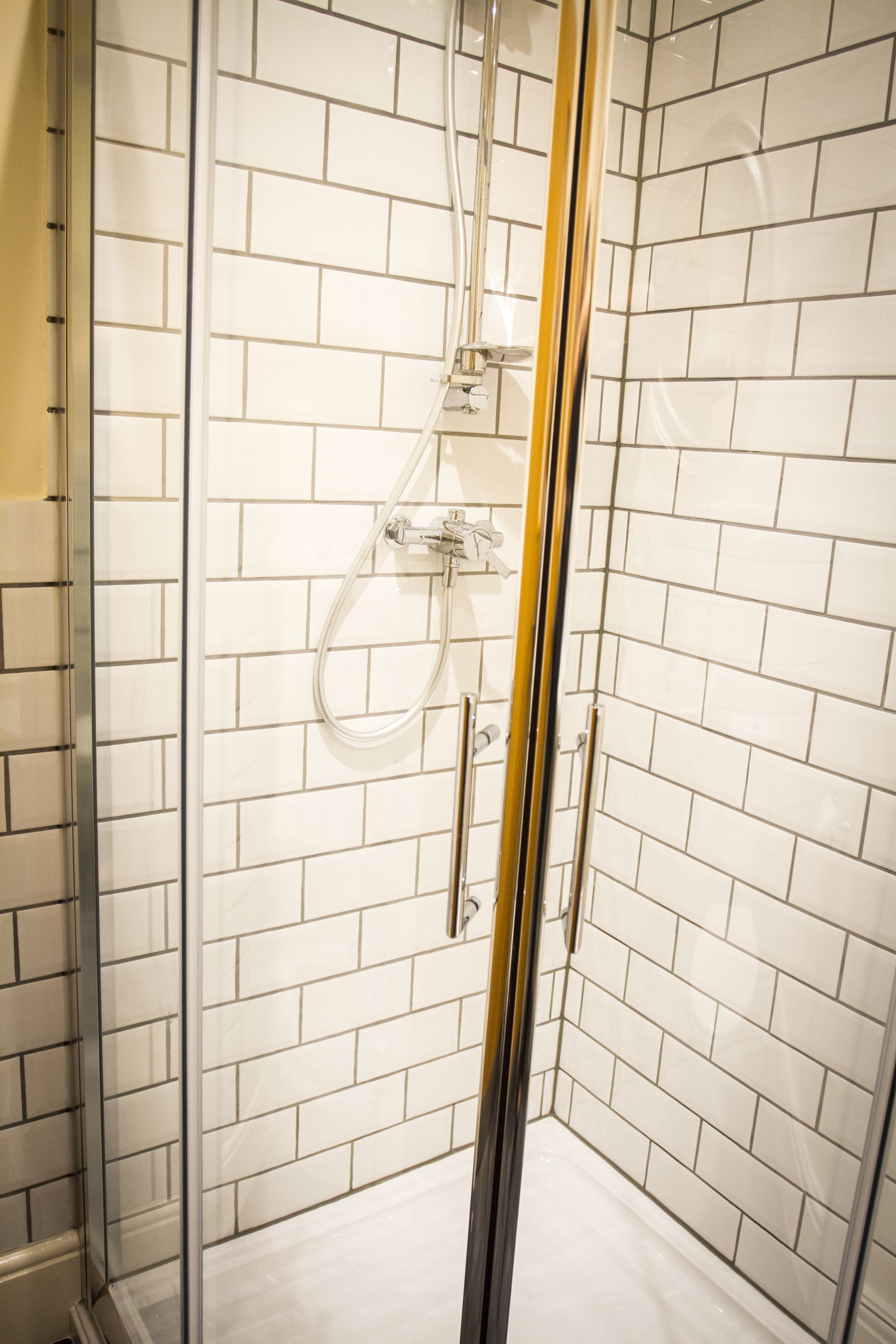 Une douche entièrementClose avec des murs recouverts de carreaux blancs et une porte en verre transparent.