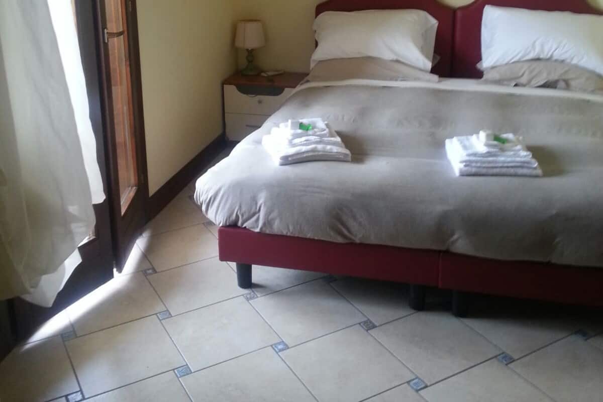 A neatly made bed with white and red bedding, a nightstand with a lamp, and a painting on the wall.