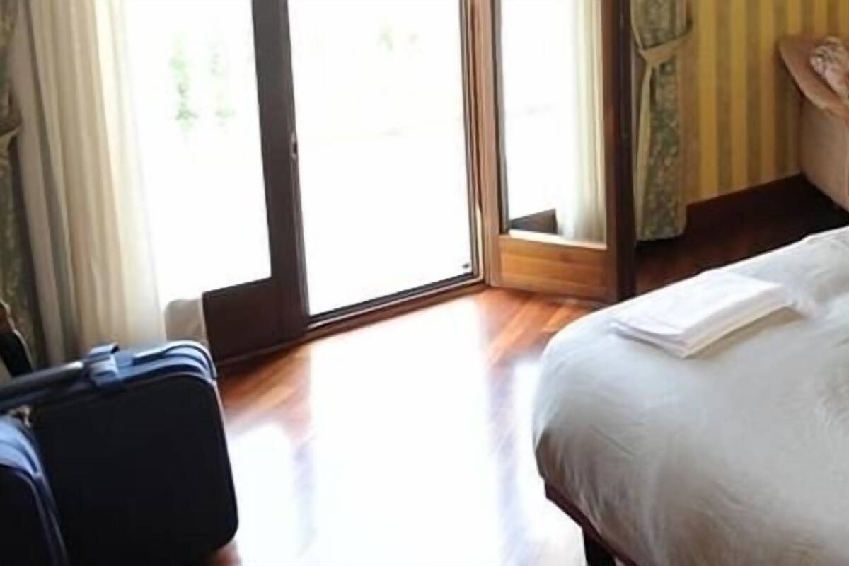 A hotel room with a bed, a chair, a desk, and a suitcase.