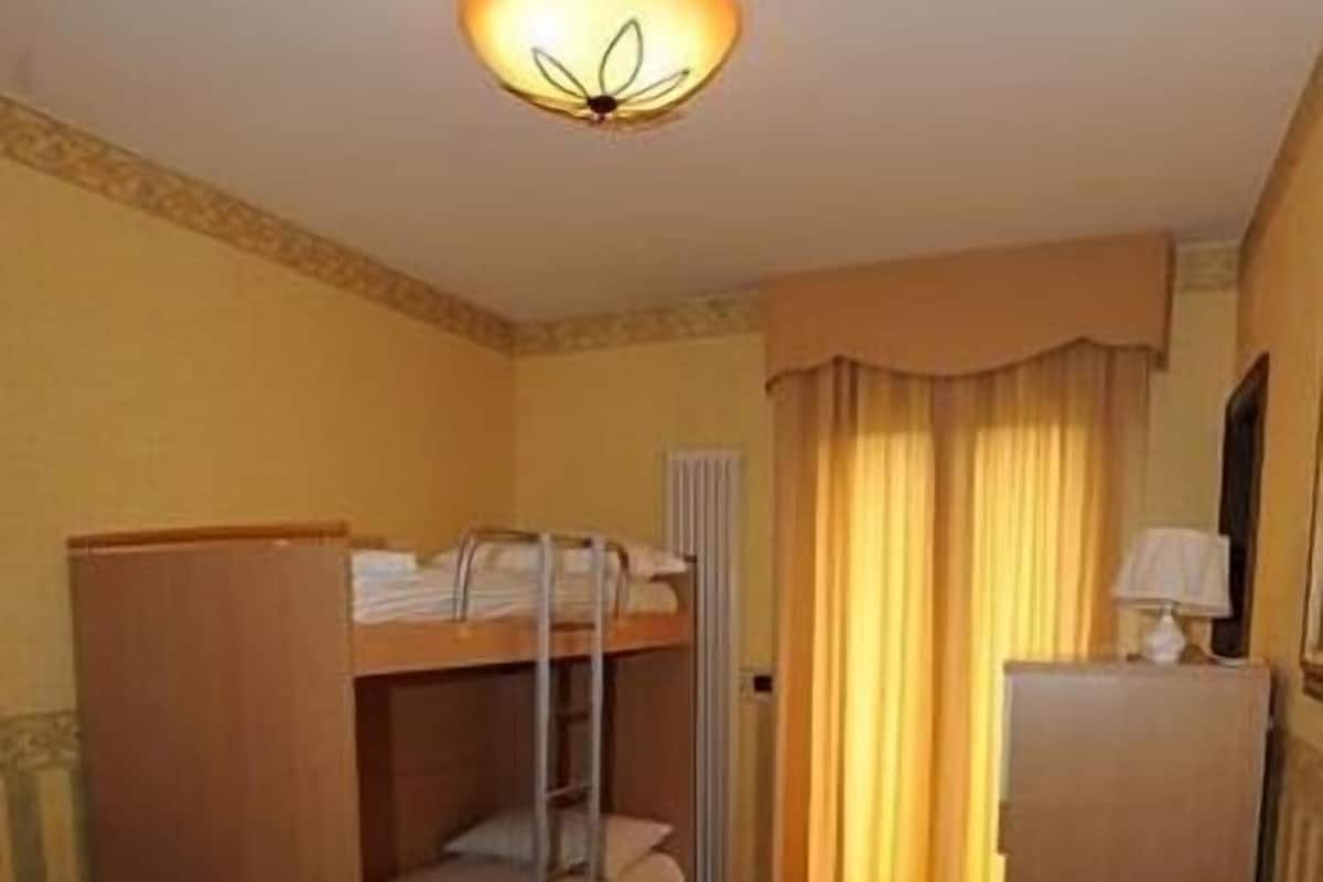 A compact room with a bunk bed, a small desk, a lamp, and a radiator.