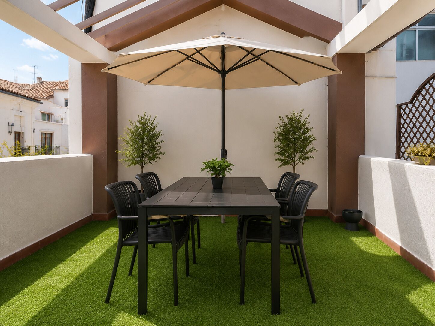 An outdoor patio with a table and chairs, a large umbrella, and artificial grass.