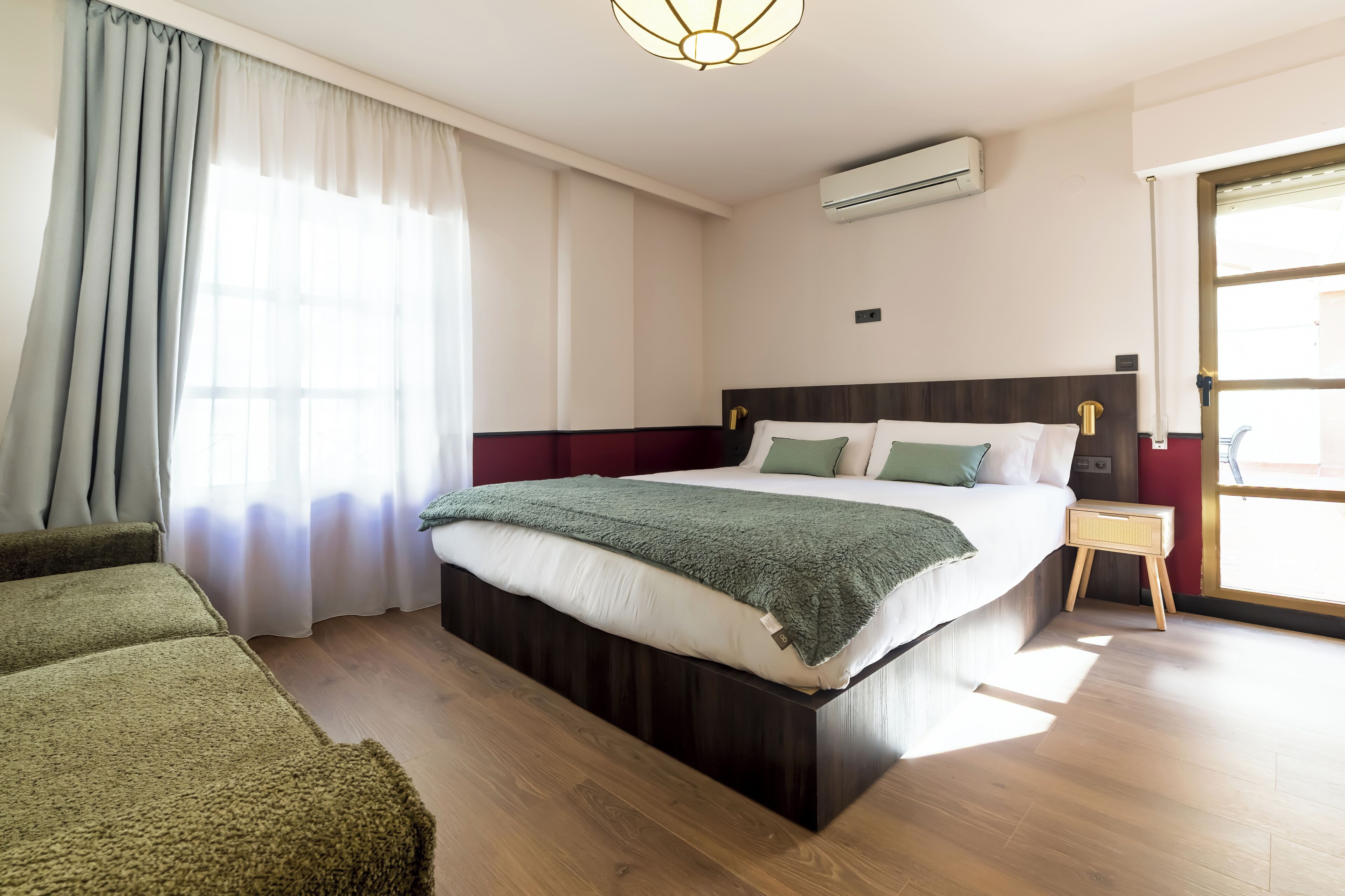 A modern hotel room with a large bed, a bedside table, a wardrobe, and a window with curtains.