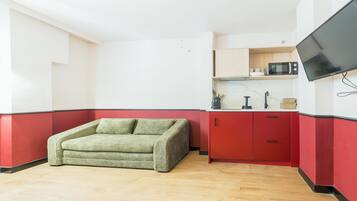 Un espace de vie compact avec un canapé vert, des meubles rouges, un four à micro-ondes et un téléviseur à écran plat fixé au mur.