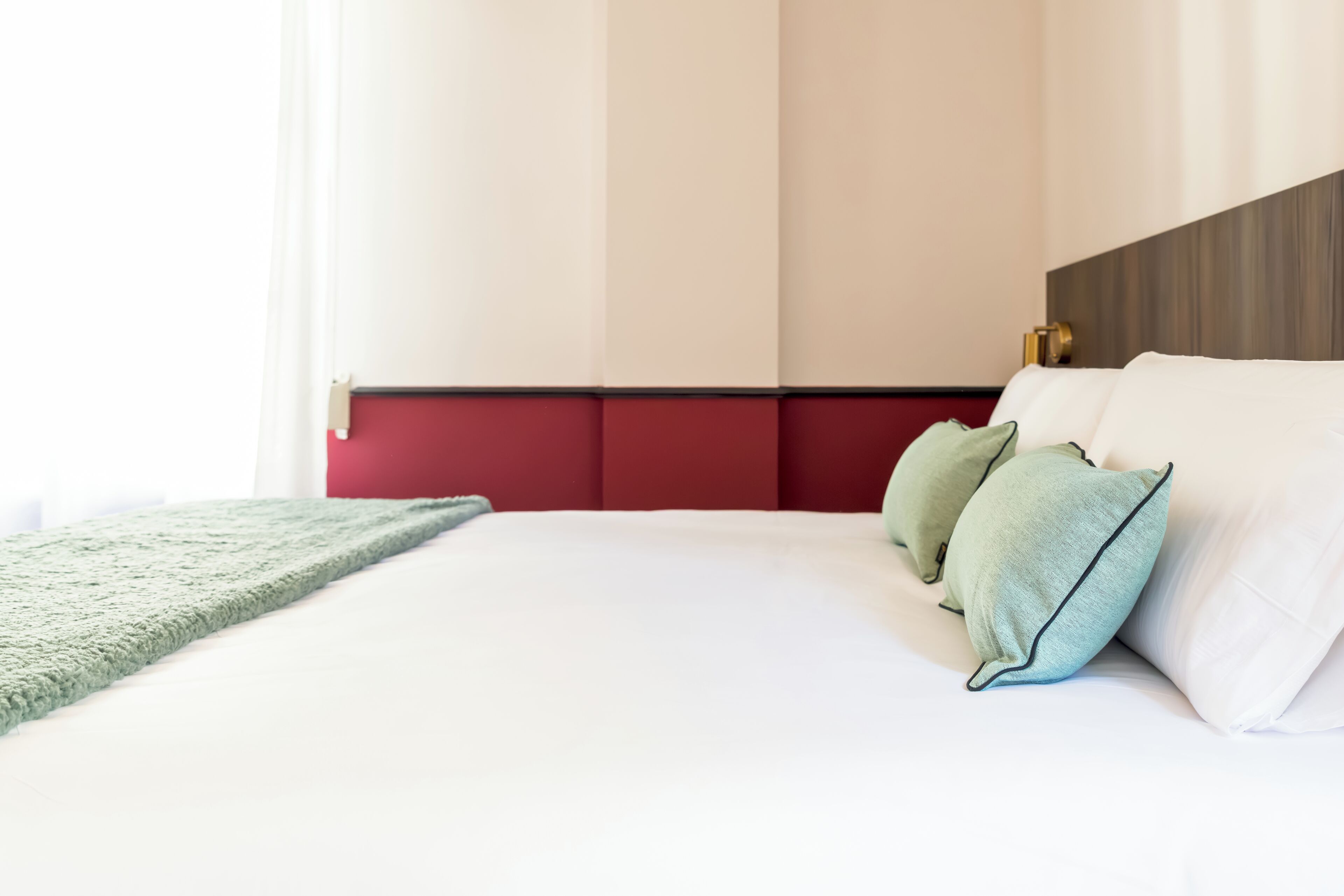 A neatly made bed with white linens and green pillows, a red headboard, and a green throw blanket.