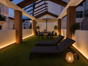 Un patio al aire libre con una mesa y sillas, dos sillones de descanso y una lámpara decorativa.