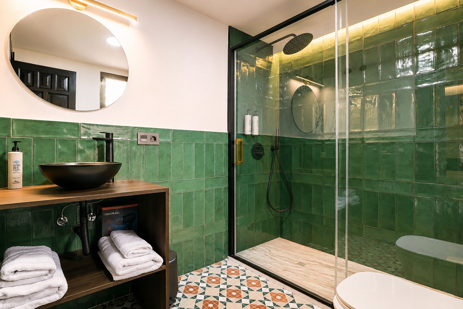 Un bagno con uno specchio rotondo, un lavabo nero, una cabina doccia in vetro e pavimento piastrellato.