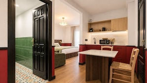 A compact hotel room with a bed, a small kitchenette, a dining area with a table and chair, and a bathroom with a shower and toilet. - Casa Lavanda by Blossom Hotels (Granada)