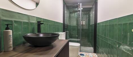 A bathroom with a large black basin, a toilet, and a shower area.