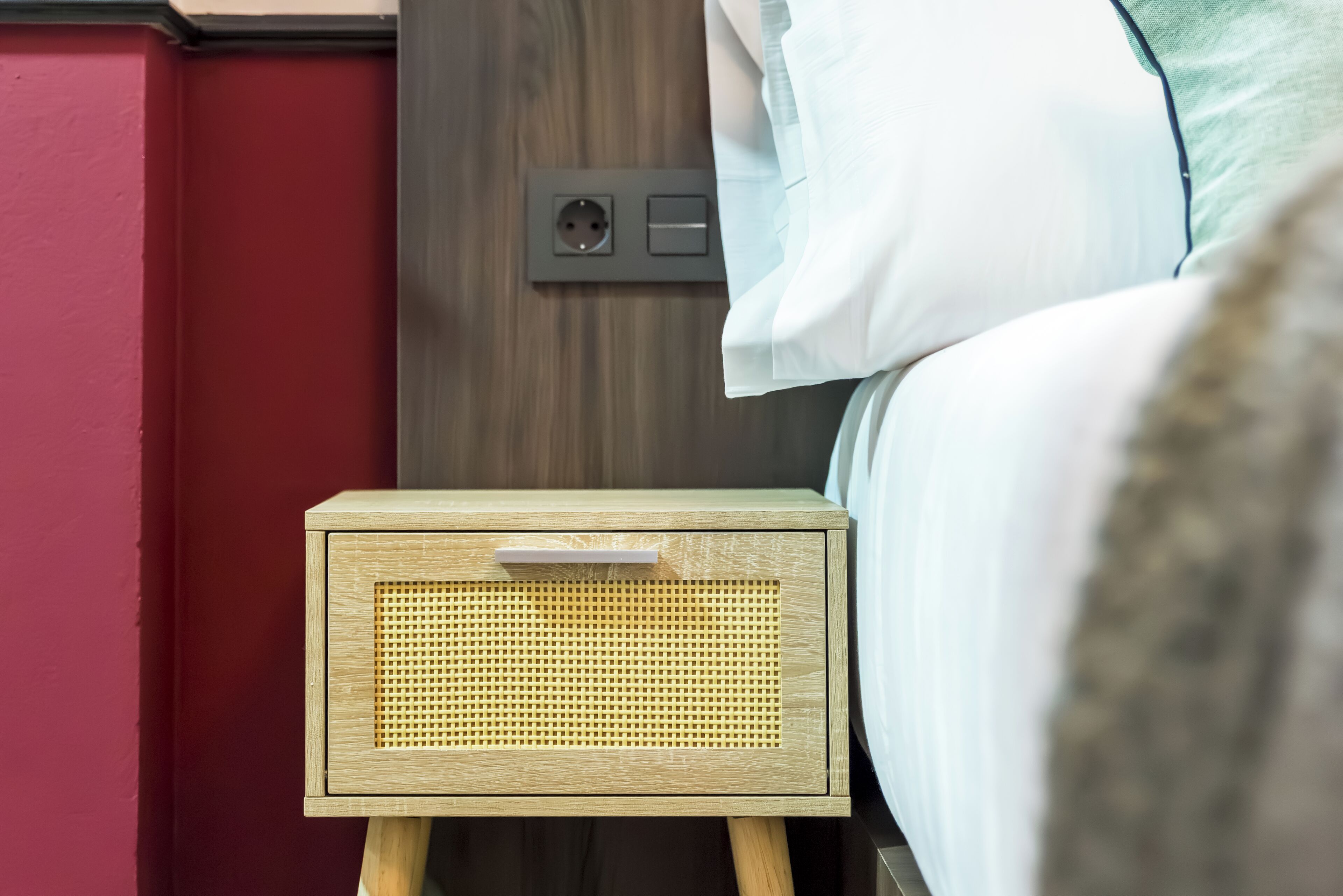 Una mesita de noche de madera con un altavoz tejido, un enchufe y un interruptor en la pared.