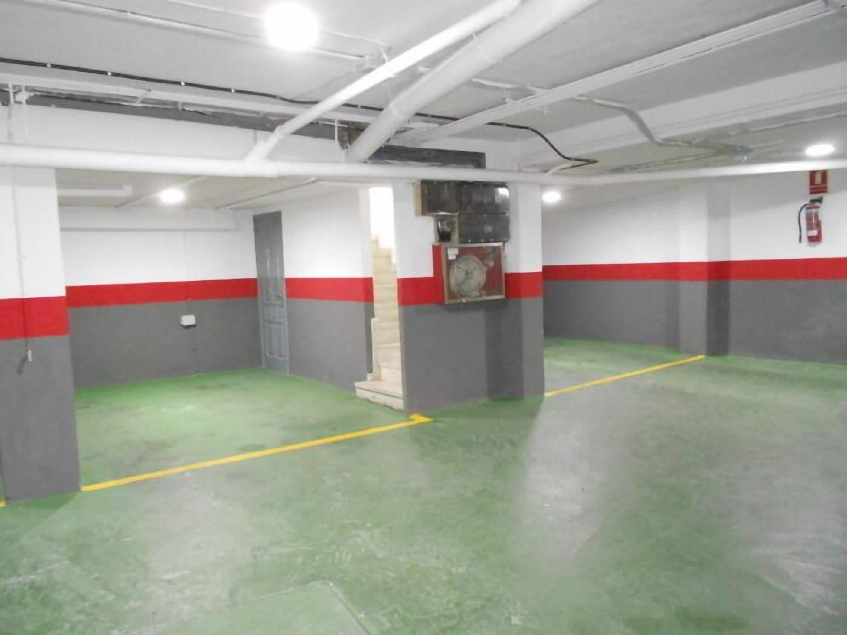 A clean, well-lit indoor parking area with green flooring and red and grey walls.