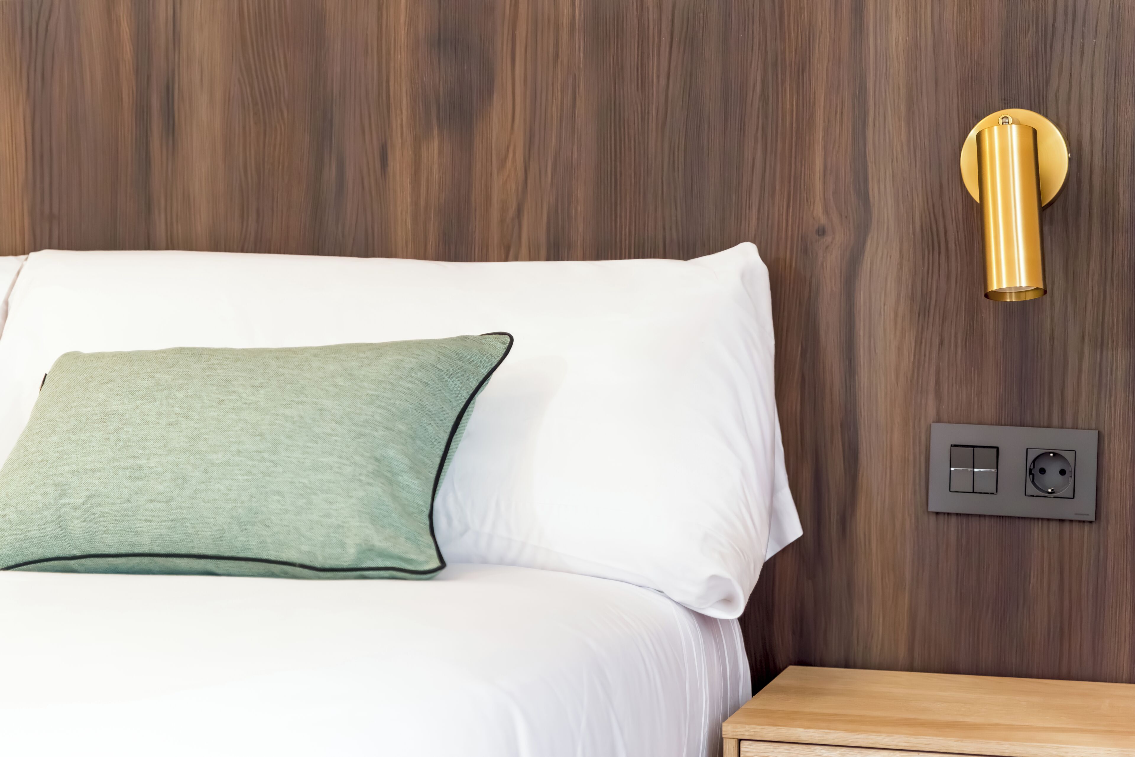 Een bed met witte en groene kussens, een houten wand en een gouden lamp.