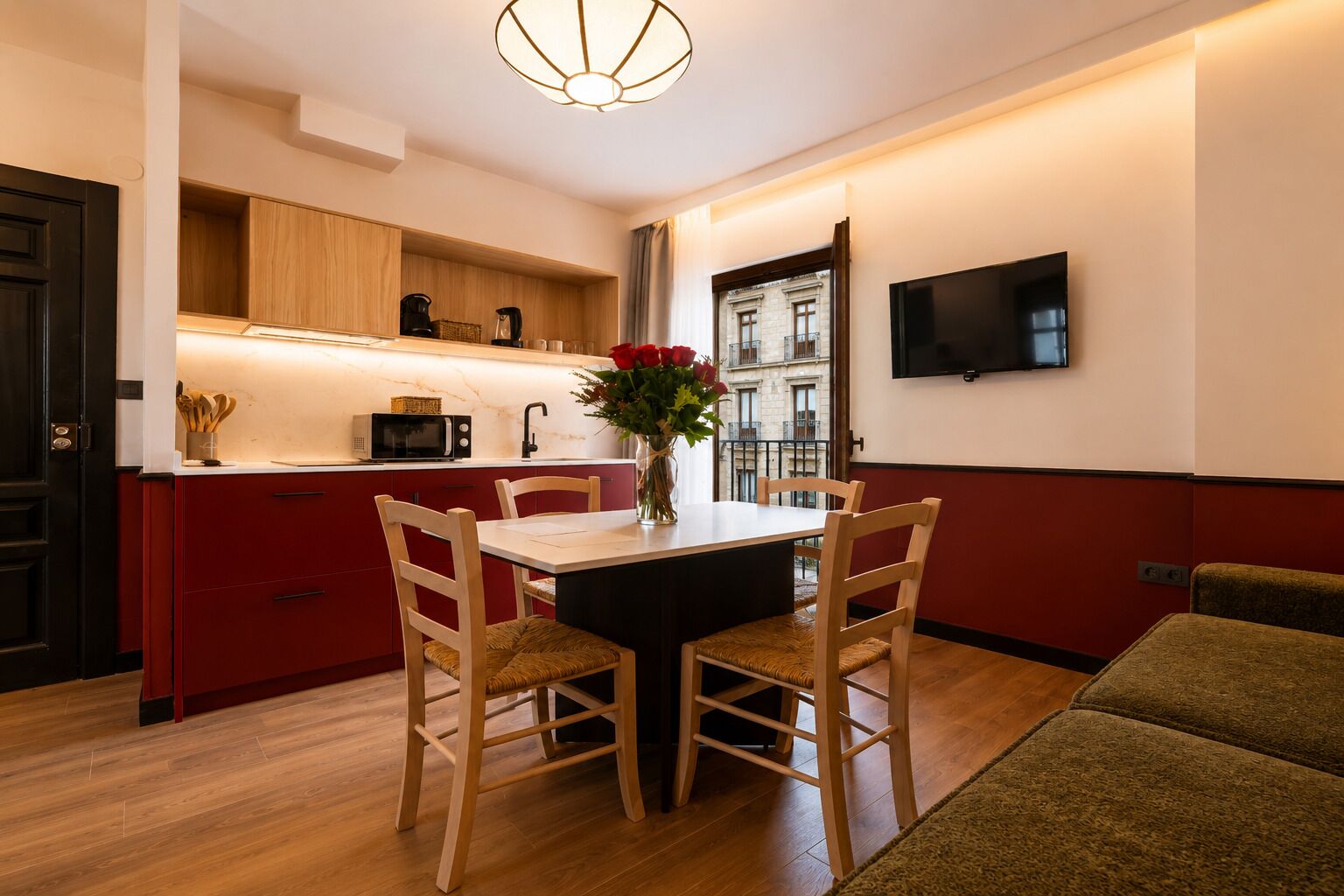 Una cocina moderna con armarios de madera, una mesa de comedor con sillas, un jarrón con flores y un televisor montado en la pared.