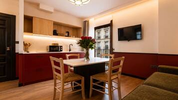 Una cocina moderna con armarios de madera, una mesa de comedor con sillas, un jarrón con flores y un televisor montado en la pared.