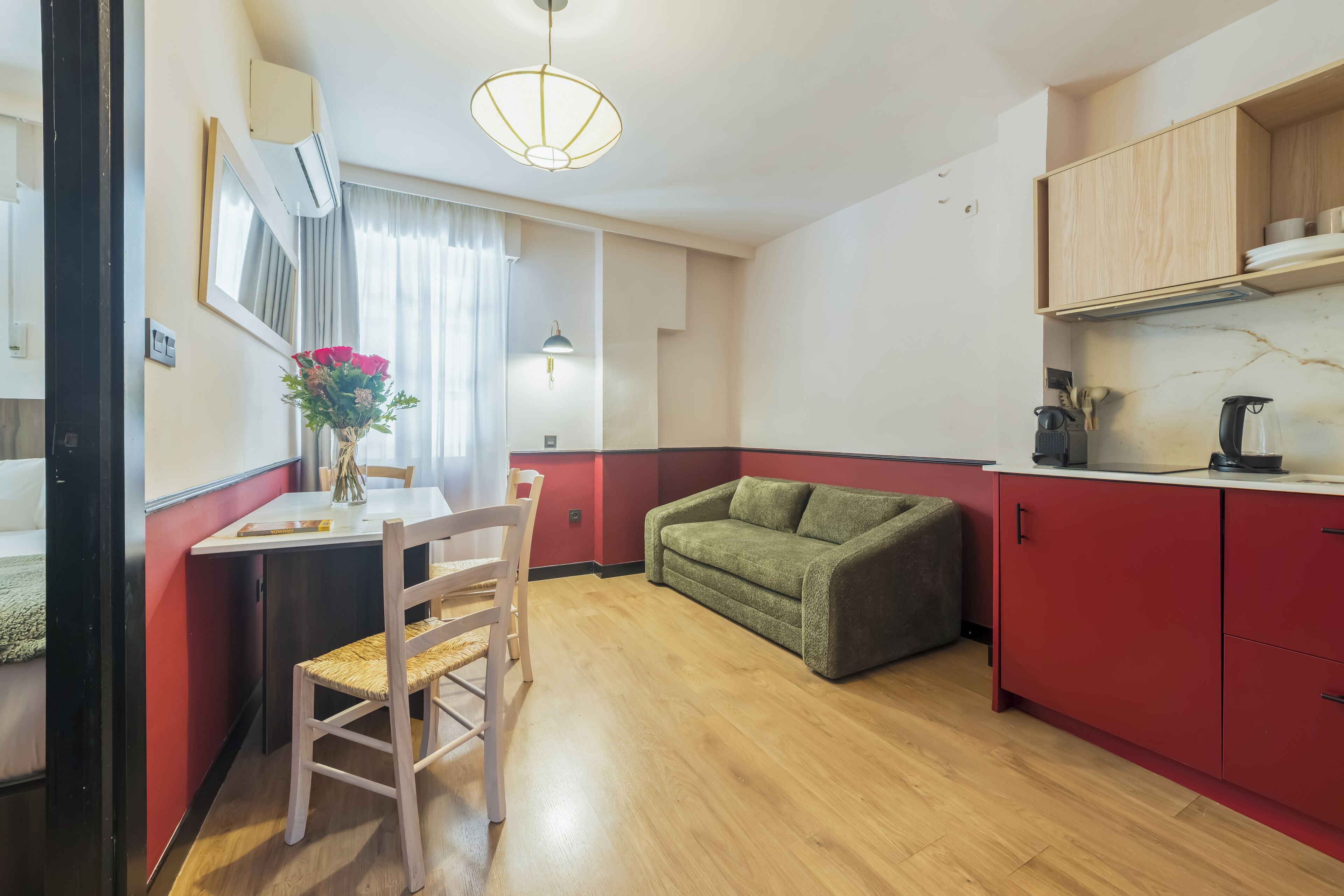 A compact kitchen with a dining table, chairs, a green sofa, and wooden cabinets.