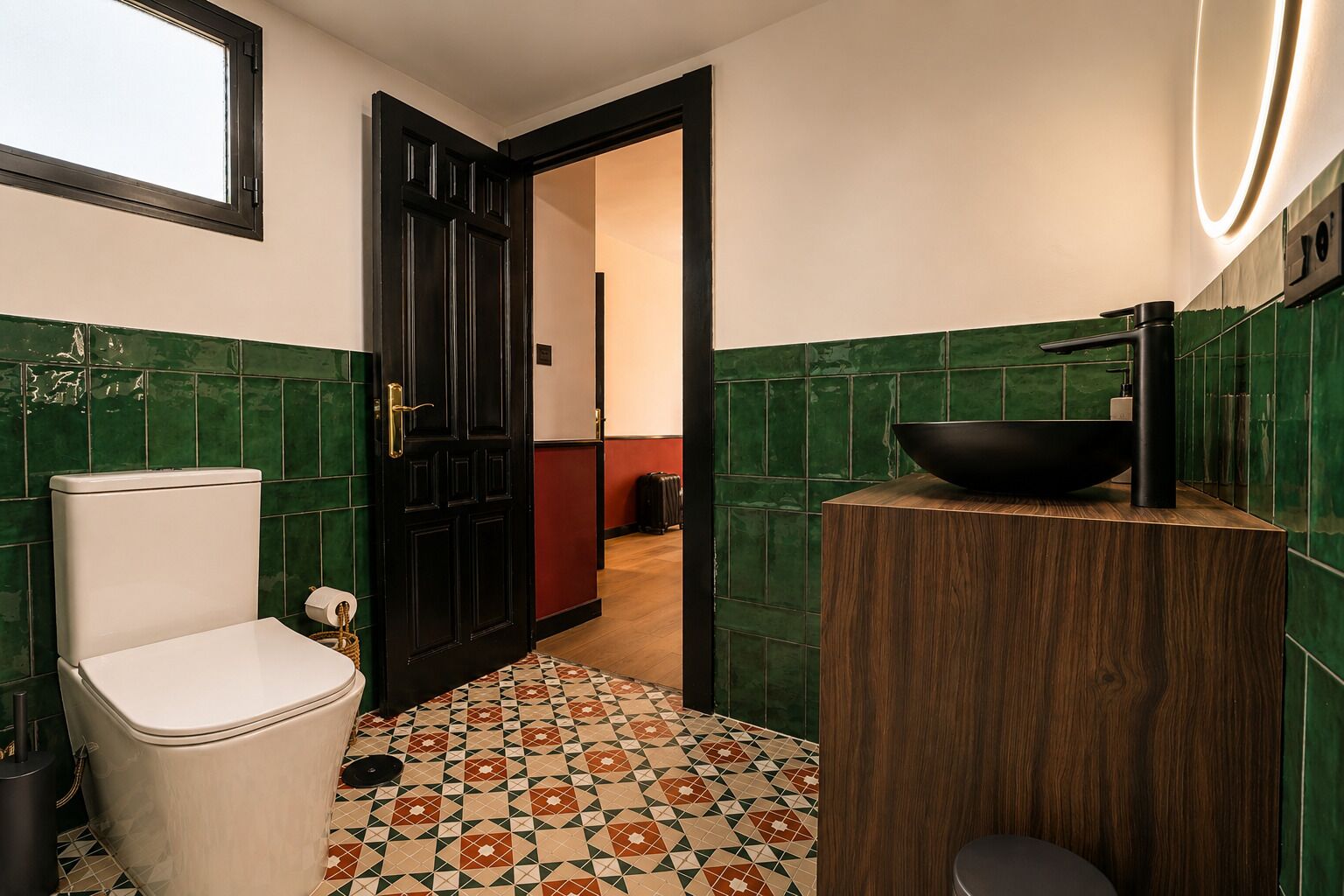 Une salle de bain avec des toilettes, un lavabo doté d’un receveur noir et un carrelage à motifs.
