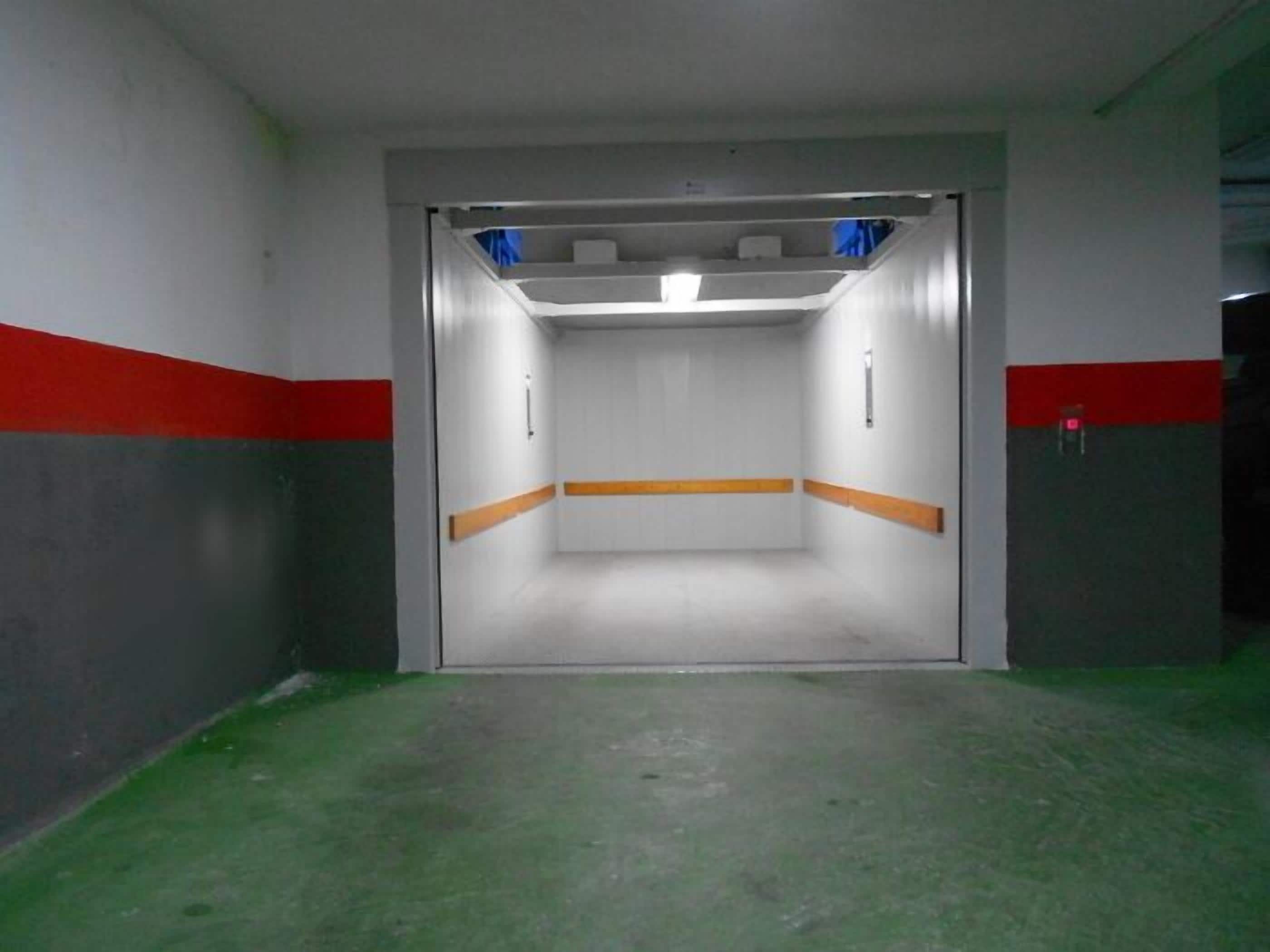 A narrow, enclosed elevator shaft with a green floor, white walls, and red stripes.