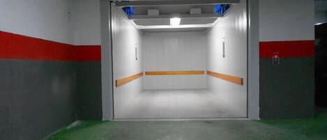A narrow, enclosed elevator shaft with a green floor, white walls, and red stripes.