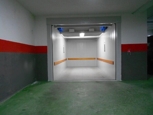 Un hueco de ascensor estrecho y cerrado con suelo verde, paredes blancas y franjas rojas.