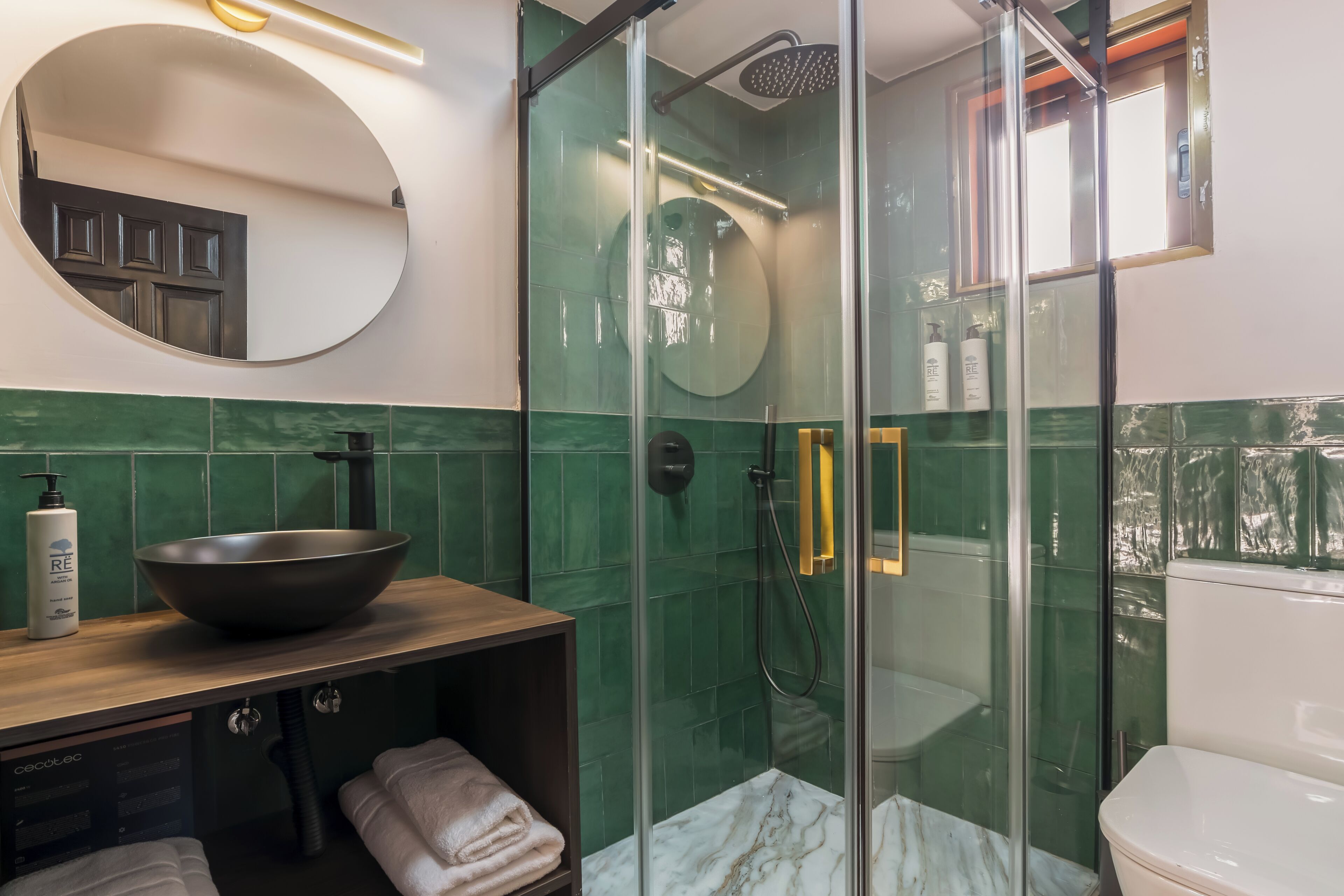 Un baño moderno con ducha de vidrio, espejo redondo y tocador de madera con lavabo.