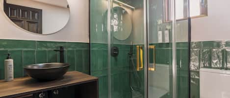 A modern bathroom with a glass-enclosed shower, a round mirror, and a wooden vanity with a bowl sink.