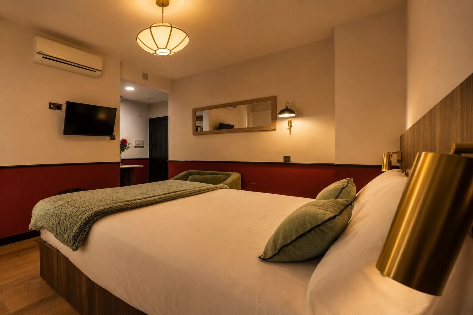 Et hotelværelse med seng, tv, aircondition, spejl og lampe.