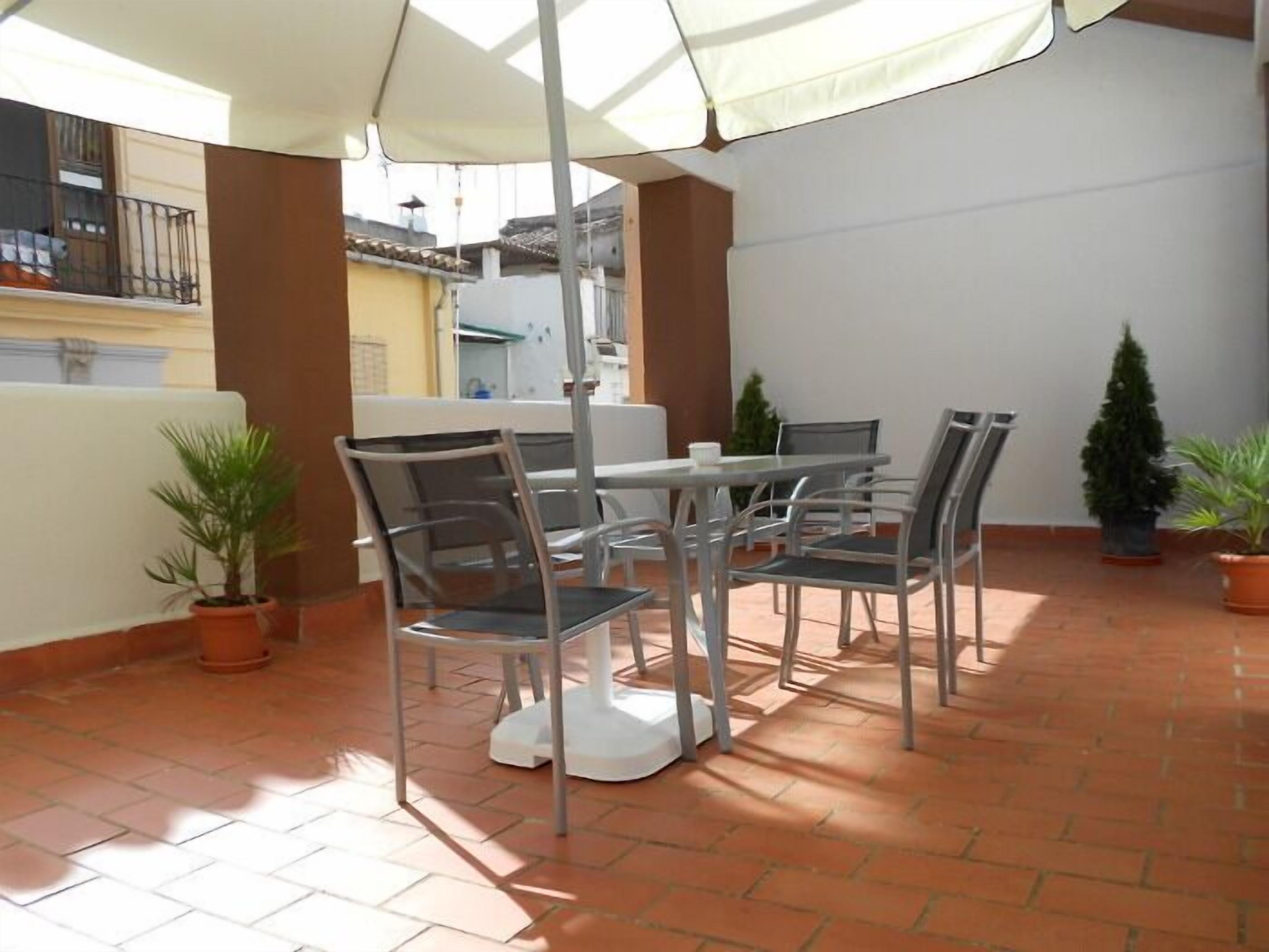 An outdoor patio with a table and chairs, surrounded by potted plants.