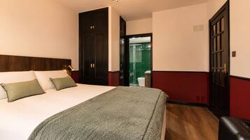 Une chambre d’hôtel avec un lit, une lampe de chevet, une tête de lit en bois, un mur rouge et blanc, et une porte donnant sur une salle de bain.
