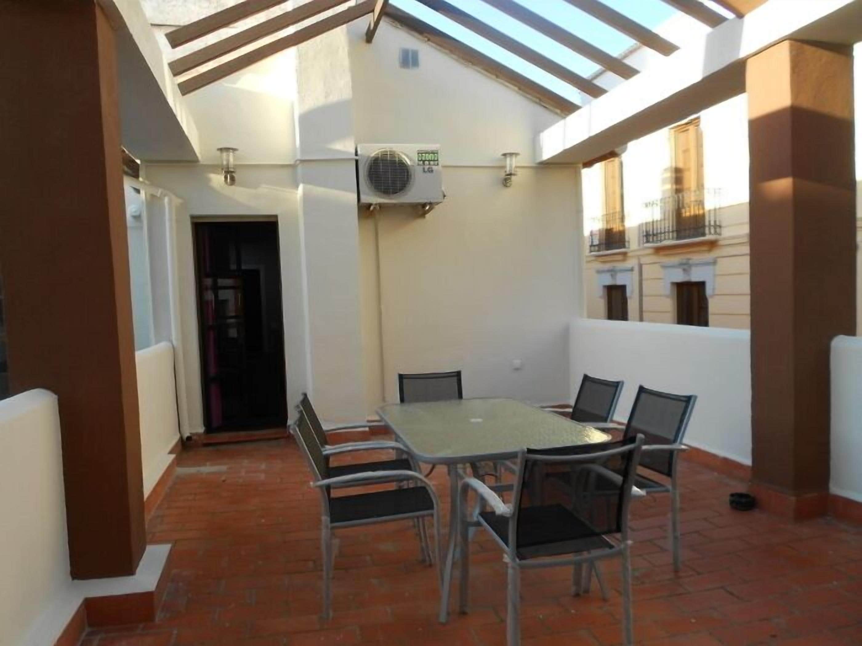 An outdoor patio with a table and chairs, an air conditioning unit, and a view of the surrounding buildings.