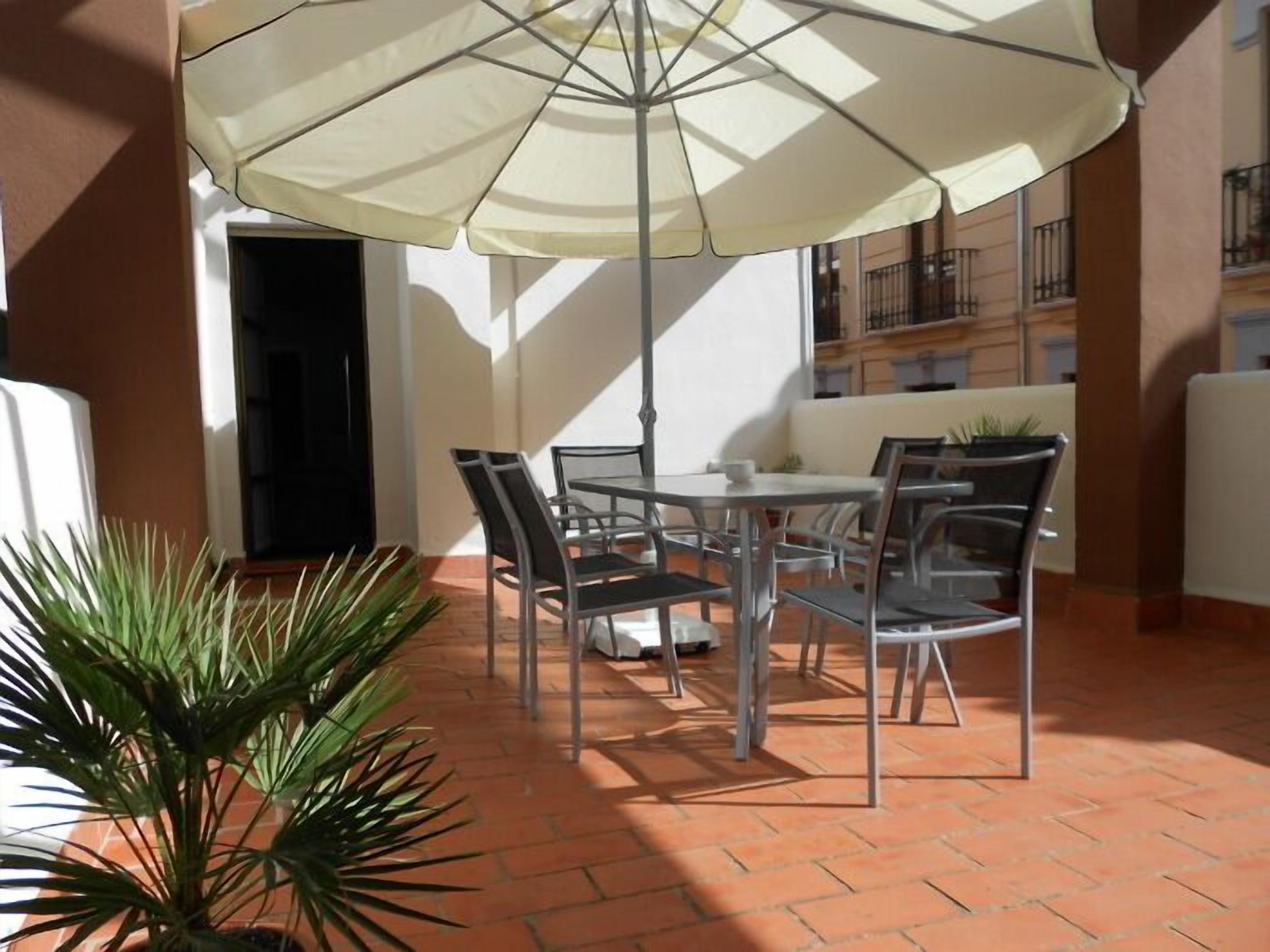 An outdoor patio with a round table and chairs, a large umbrella, and a potted plant.