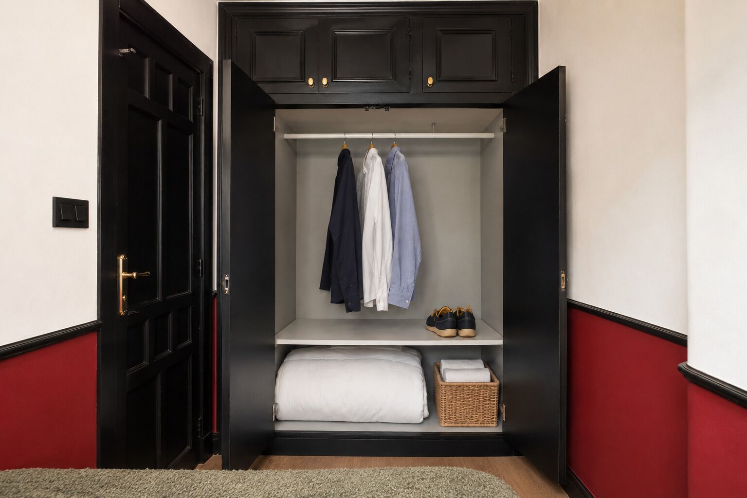 A walk-in closet with hanging clothes, a shelf with shoes, and a bed with a white comforter.