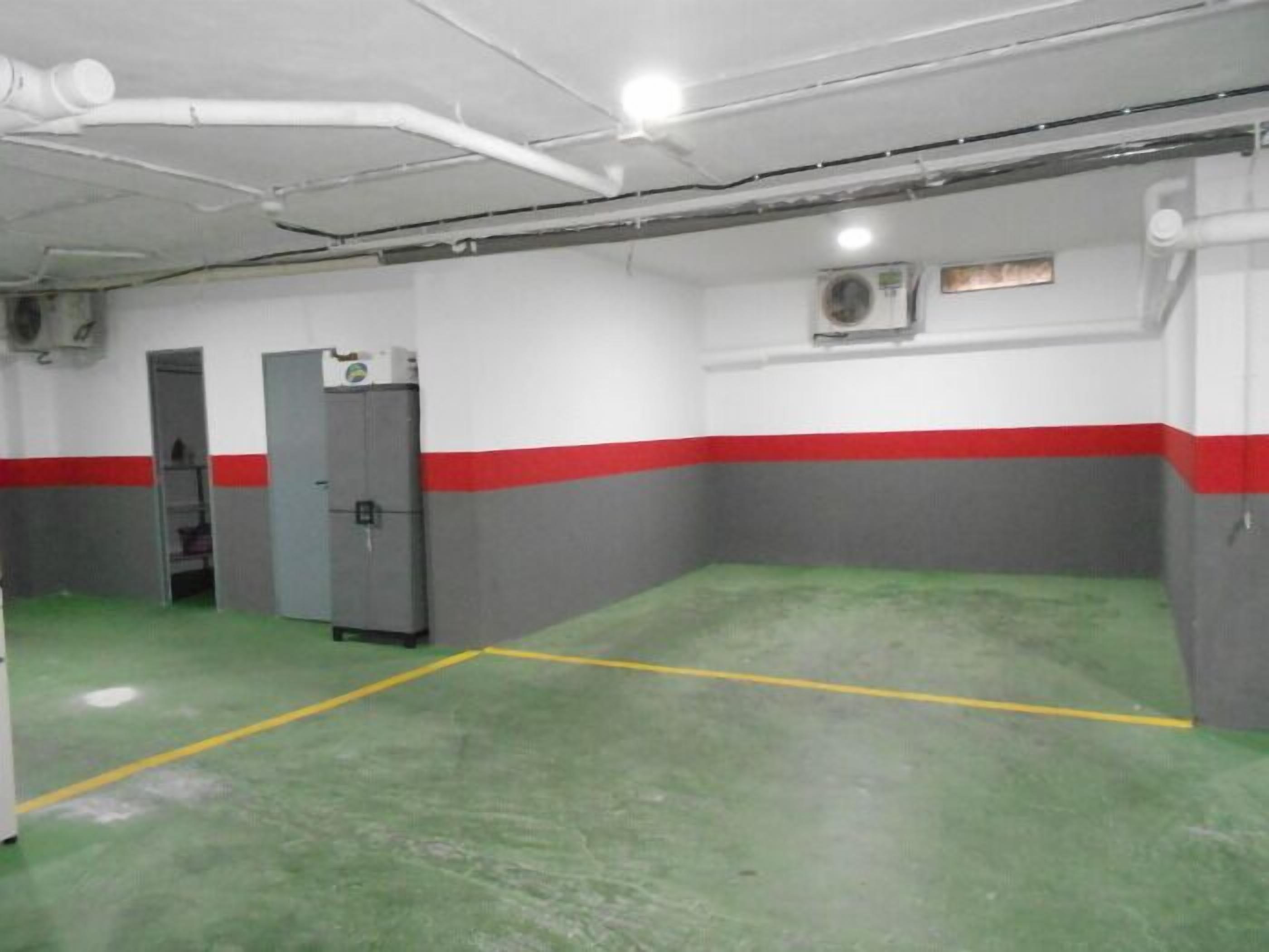 A spacious indoor area with a green floor, white walls with red stripes, and a grey door.