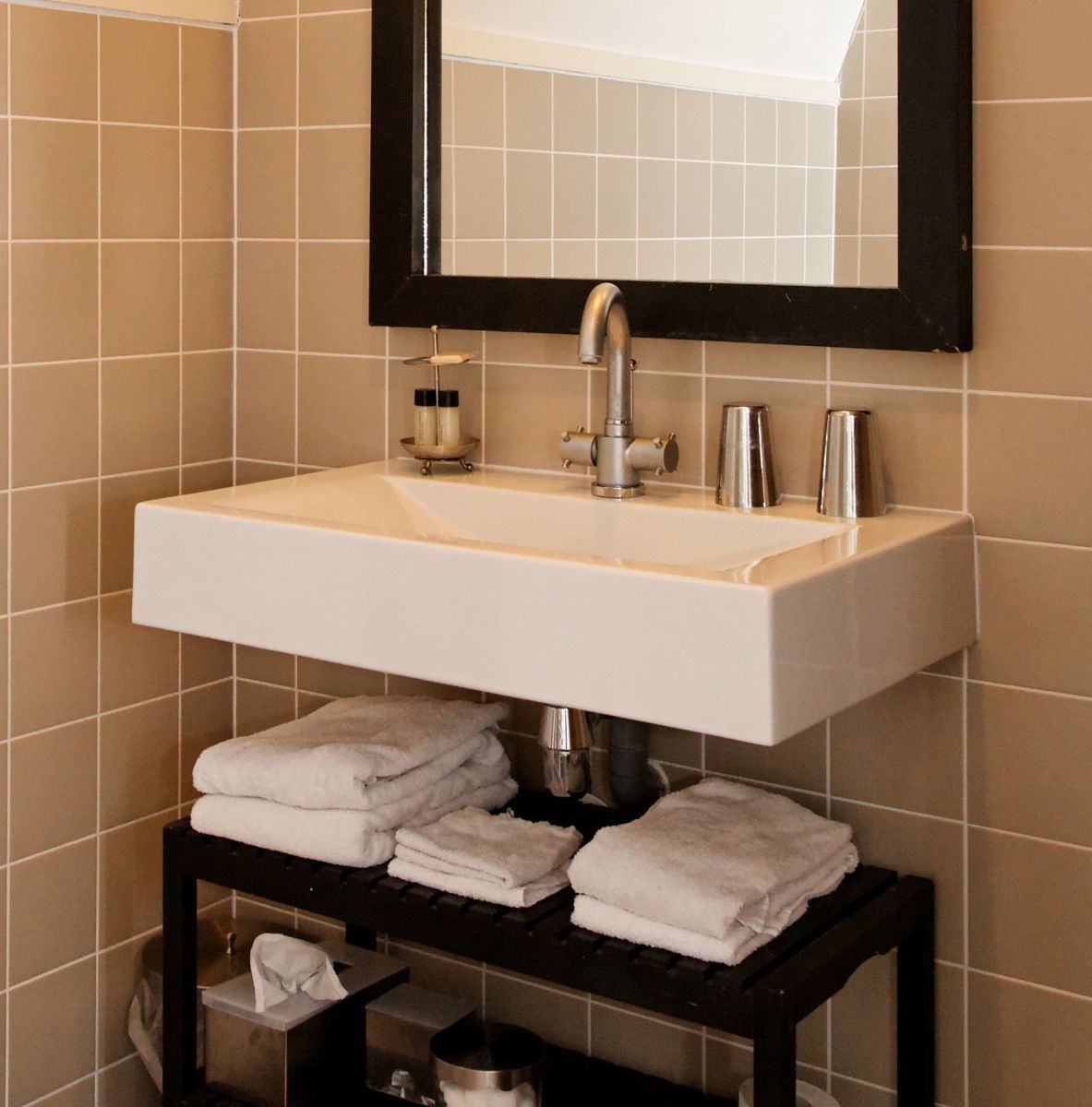 A bathroom with a white sink, a black-framed mirror, and a shelf with folded towels.