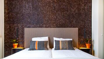 A double bed with two pillows, a brick-patterned wall, and two nightstands with potted plants.