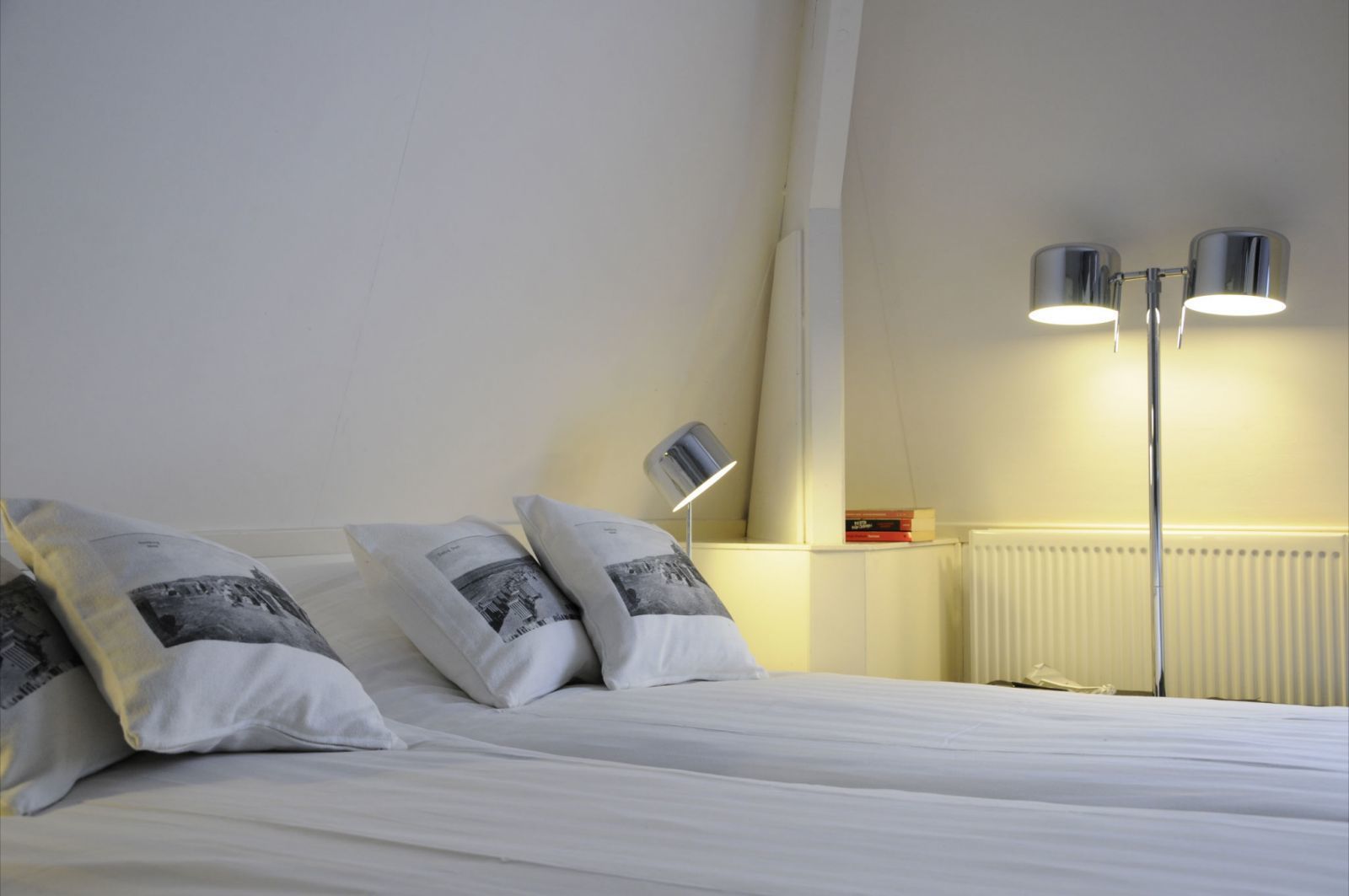 Una habitación de hotel con una cama bien hecha, dos lámparas de noche y un radiador.