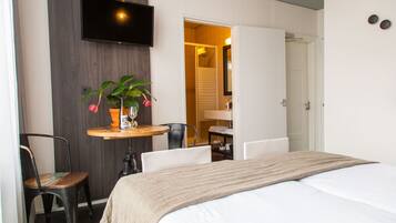 Ein Hotelzimmer mit Bett, Wandfernseher, einem kleinen Tisch mit Pflanze und einem Sessel.