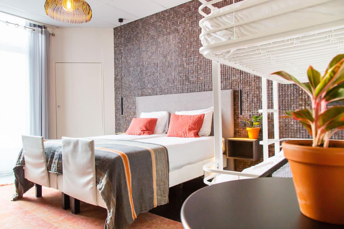 Une chambre d’hôtel moderne avec un grand lit, une table de chevet, une plante en pot et une vue sur l’extérieur.