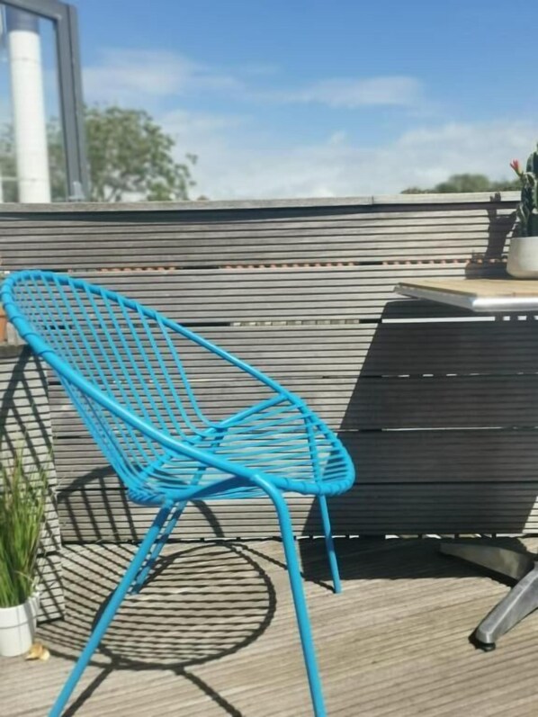A blue metal chair on a wooden deck with a black table and a potted plant. - Hotel Pannenkoekhuis Vierwegen (Domburg)