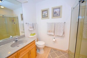 A bathroom with a glass shower enclosure, a sink with a mirror, a toilet, and two framed pictures on the wall. - Harbour Island 403m 2 Bedroom Condo by RedAwning (Ocean City)