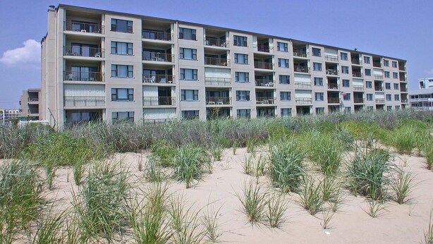 Ein mehrstöckiges Hotel mit Balkonen in der Nähe eines sandigen Strandes mit Vegetation.